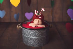 Newborn baby in a bucket with a love monster hat surrounded by floating hearts