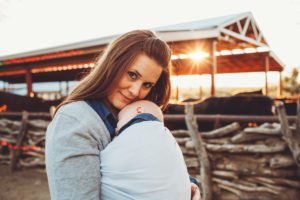 A young mom cuddles her baby boy to her while he sleeps in her arms as the visit the horse corral at Tanque Verde Guest Ranch