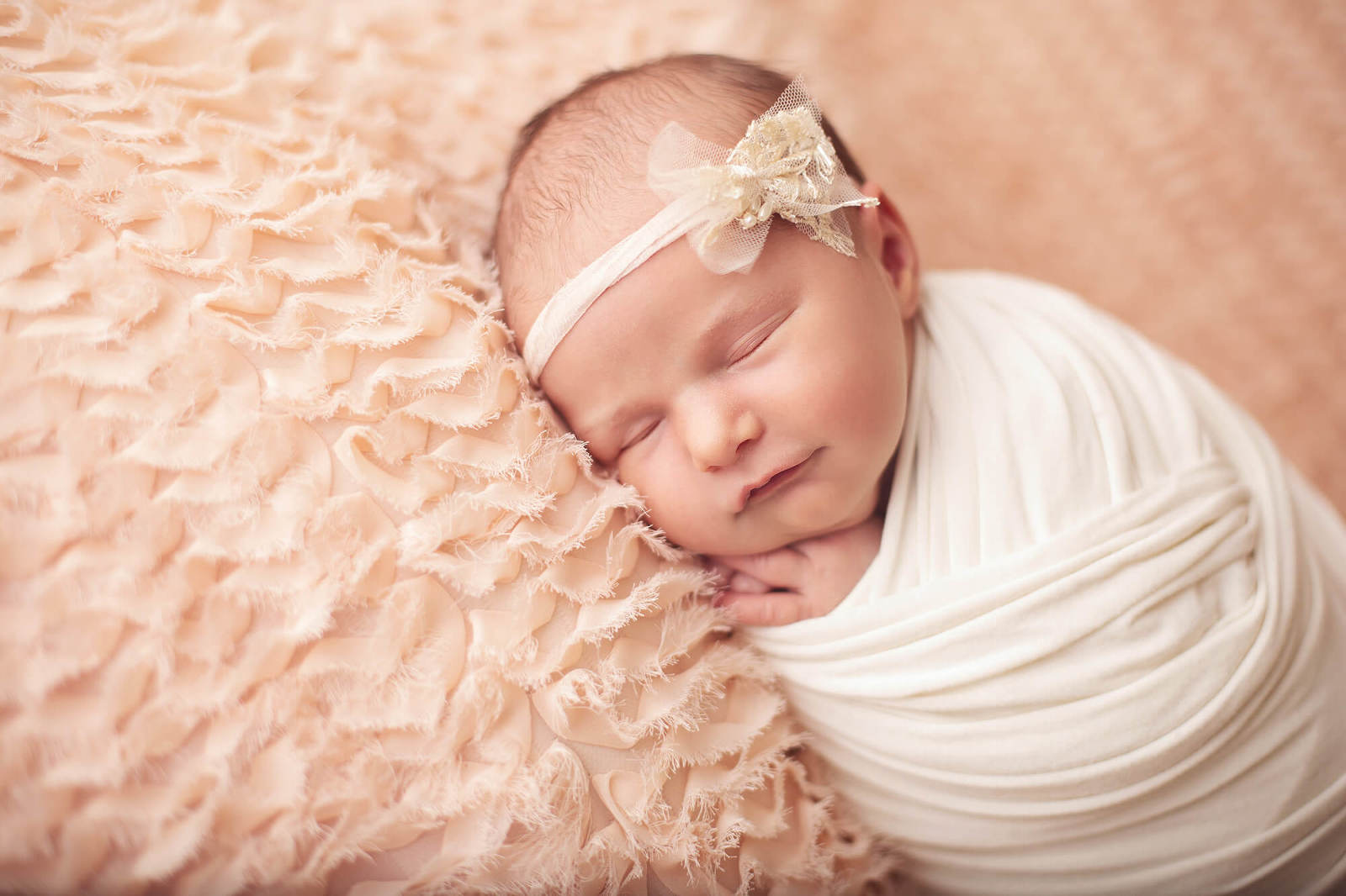 Newborn baby girl smiling with a pearl bow headband during her Tucson newborn session