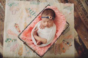 Newborn baby girl wrapped and laying in a wire basket over a quilt by Clay Kaserne newborn photographer