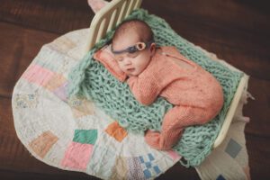 newborn girl in a peach onesie laying on a bed by Hainerberg newborn photographer