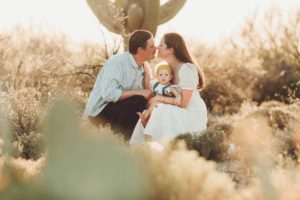 A family of three with mom and dad about to embrace holding their baby daughter under a giant saguaro in Tucson