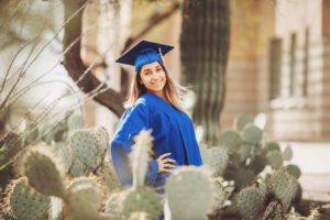 A senior at Catalina Foothills High School poses amongst cactus and desert fauna at her school in her cap and gown