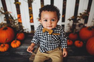 Little boy during his one-year studio studio session with a fall fence and baby pumpkins