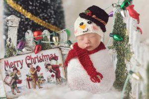 Newborn in a snowman costume sitting next to a Christmas decorated fence by Tucson newborn photographer Belle Vie Photogrpaphy