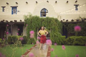 A woman poses in a hotel courtyard surrounded by flowers and greenery during her glamour session at Hacienda Del Sol.