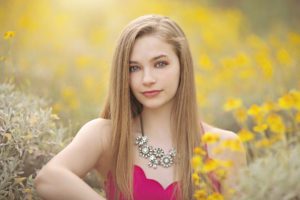 A young woman poses amongst the yellow spring desert flowers during her senior photoshoot with Belle Vie Photography