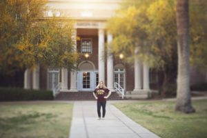 A class of 2018 senior stands in front of a college dorm wearing her Arizona State University t-shirt