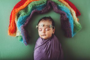Newborn baby girl wrapped in purple with a rainbow scarf over her head
