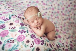 Newborn baby girl on a lavender and pink backdrop with a delicate green velvet bow