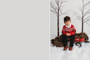 A little boy all set for a wintery Christmas sits on a wagon surrounded by snow during a holiday studio photo session with Belle Vie Photography