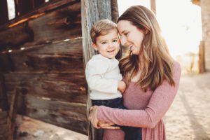 A mom holds her little boy next to a barn illuminated from behind during a family photo session in Sonoita