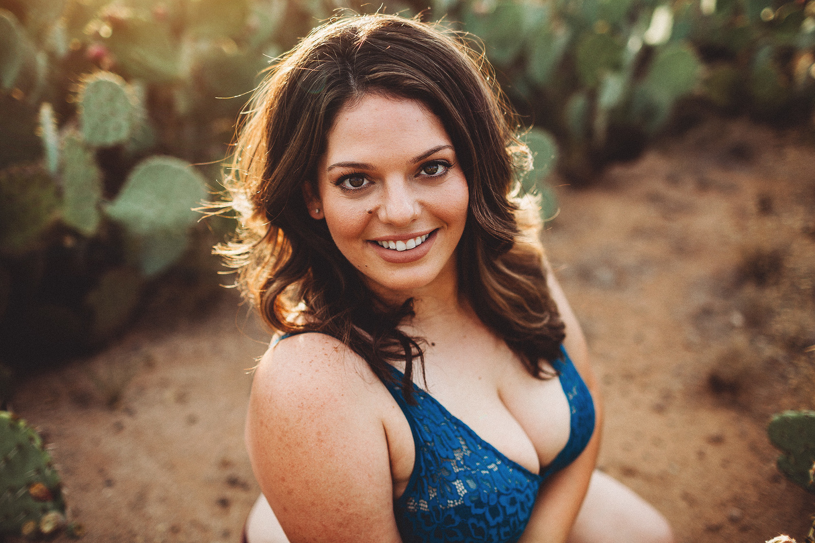 A young woman posing amongst the cactus during her sunset desert boudoir session