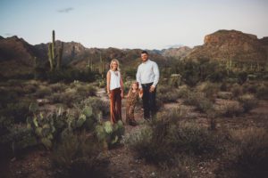 A family of three holds hands surrounded by desert and the Catalina Mountains during a sunset desert family photo session