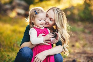 A mom snuggles her daughter as she plays with a pine cone during a fall family shoot