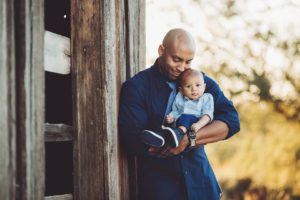 A father and his baby boy snuggle next to a barn at sunset