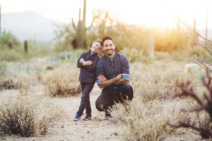 A father and son lean against one another playfully during a fun family photo session in the desert near Tucson