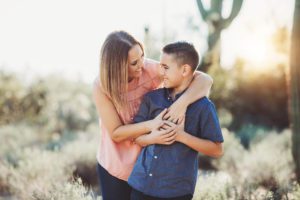 A mother hugs her first-born, tween son close to her surrounded by desert and saguaros during a family photo session at Sabino Canyon
