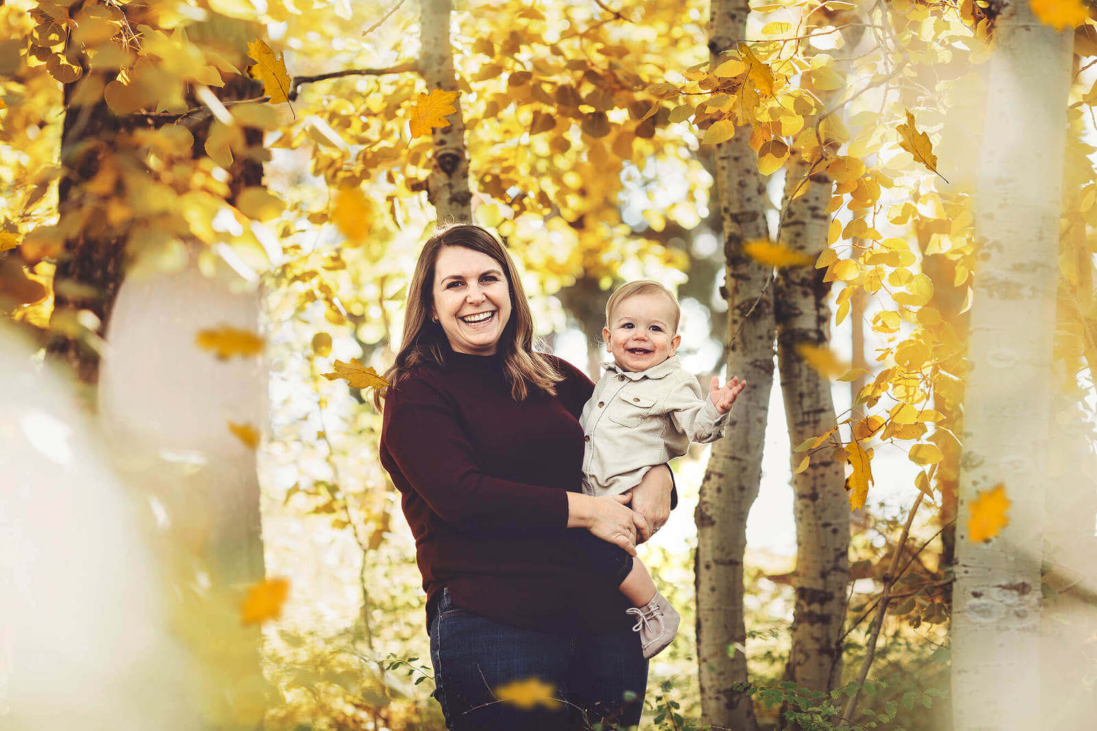 A mother and son playfully giggle surrounded by fall mountain foliage