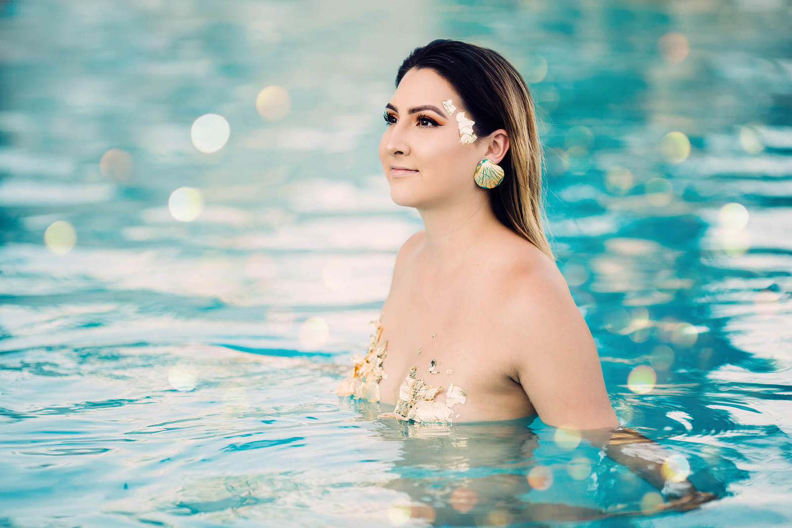 A woman covered in gold foil floats in a pool during a mermaid photoshoot at the Urban Grove in Tucson for Luna + Saya jewelry