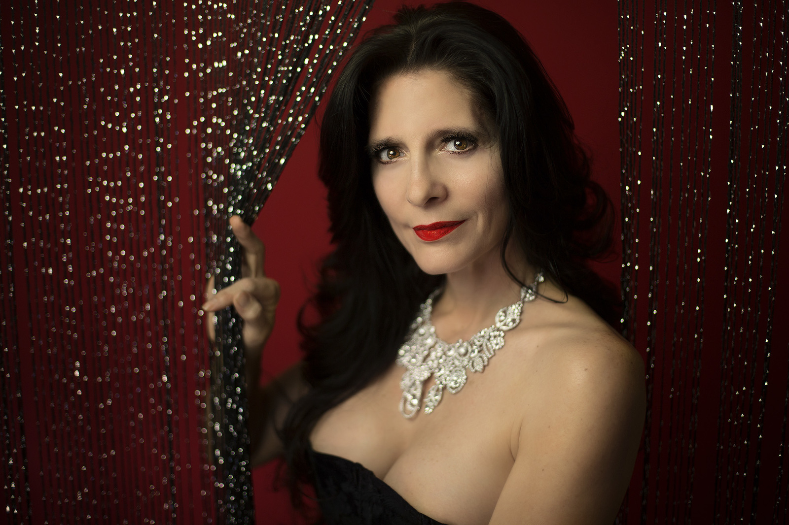 Woman wearing red lipstick against a red backdrop and black shimmer curtain for a Valentine's Day boudoir photoshoot in Tucson