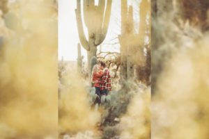 The Freeman's kiss surrounded by giant saguaros and spring desert flowers during their couple's session with Belle Vie Photography in Tucson