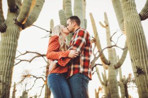 The Freeman's kiss with giant saguaros surrounding them in the warmth of the setting Tucson sun during their couple's session with Belle Vie Photography