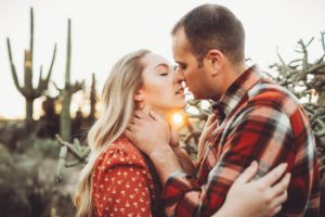 A kiss between husband and wife with the setting sun between them during their couple's session at Sabino Canyon in Tucson
