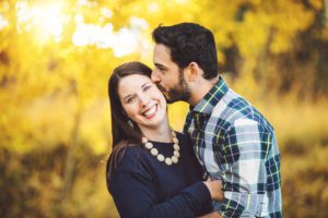 A mom and dad share a kiss surrounded by yellow fall foliage on Mt. Lemmon during their 2018 holiday photo session