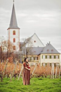 A mom in brown velvet during her maternity session with a church in Hochheim, Germany after the vineyard leaves have fallen