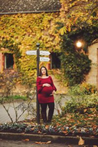 A mom during her maternity session leaning against a cute German sign near Clay Kaserne