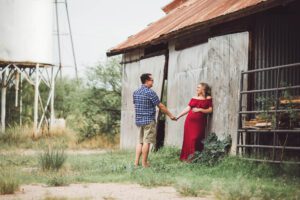 Parents-to-be gaze at each other while posing next to a barn during their maternity session in Sonoita