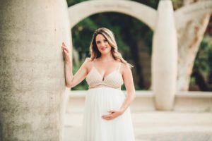A beautiful mom-to-be in a beaded white gown at sunset during her maternity session at the University of Arizona