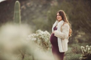 Mom-to-be Anica poses amongst desert cactus in a fur coat during her chilly sunrise maternity session