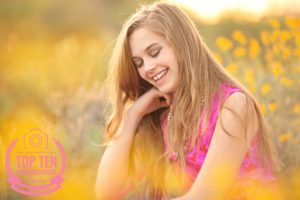 A girl laughs surrounded by yellow spring desert flowers during her senior photo session in Tucson