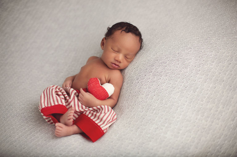 Newborn baby boy Carter holding a heart wearing red and white striped pants