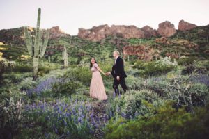 A couple walk amongst the wildflower blooms during their spring engagement session with Belle Vie Photography