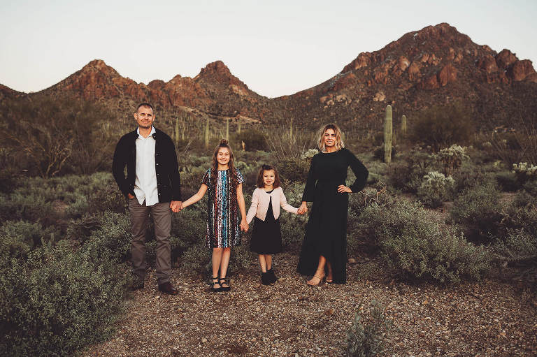 The Gunter family holding hands at sunset with the peaks of Gates Pass at their backs during their snowy desert family session