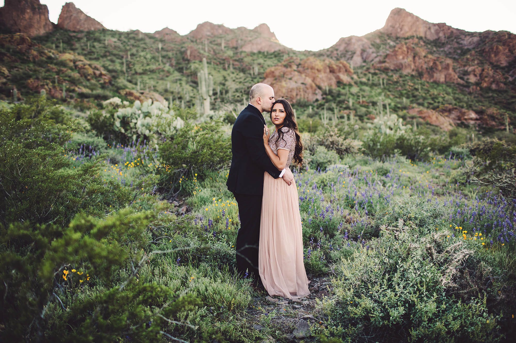 Brad kisses Vanessa surrounded by desert wildflowers during their spring couples session at Picacho Peak