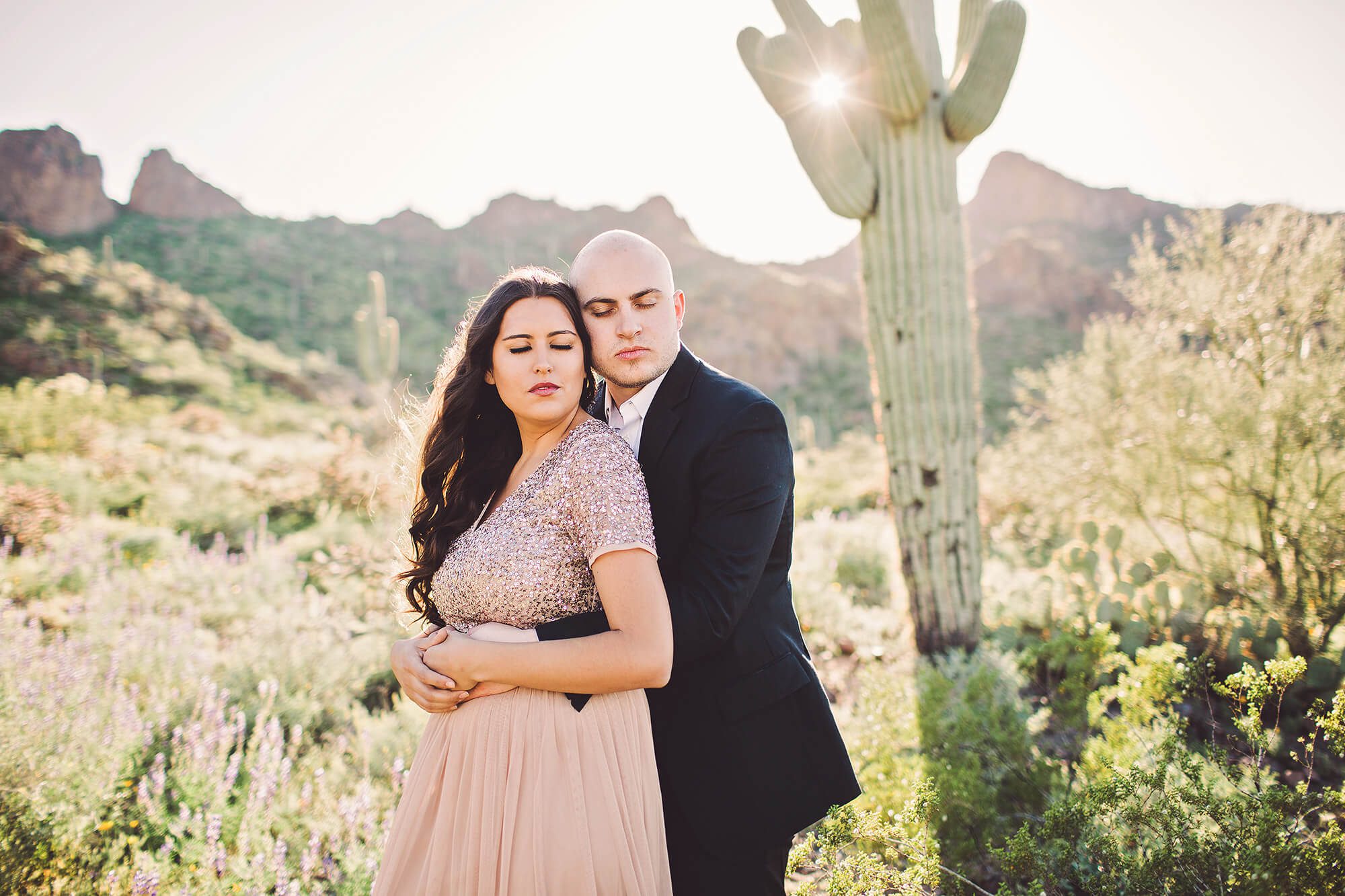 The Paxman's hold one another amidst the sun and saguaros during their Picacho Peak wildflower session
