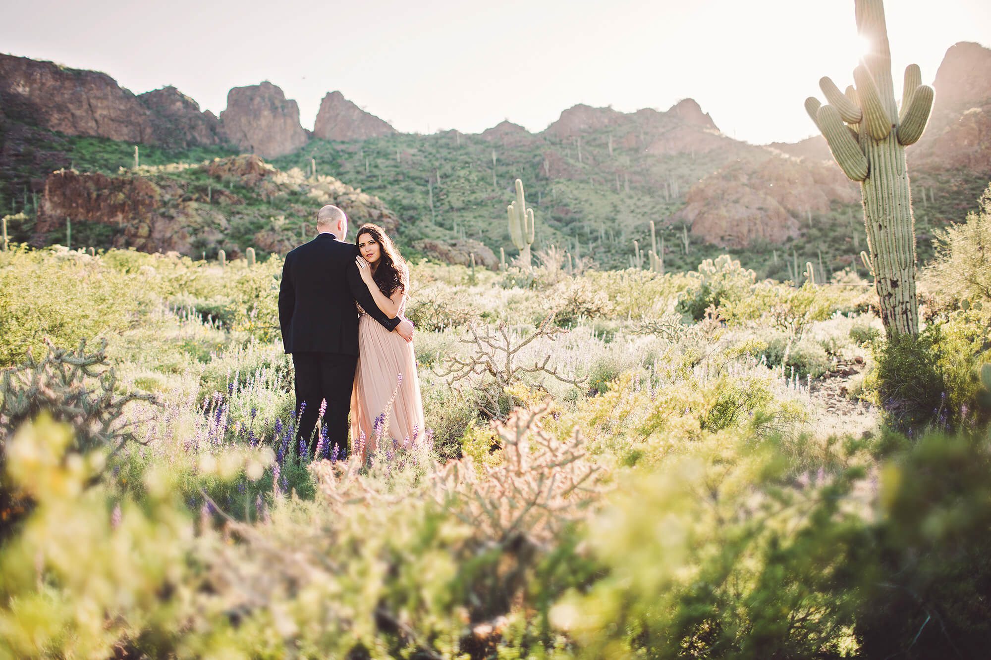Standing in the sunlight amongst the wildflowers, the Paxman's hold one another during their couple's session at Picacho Peak