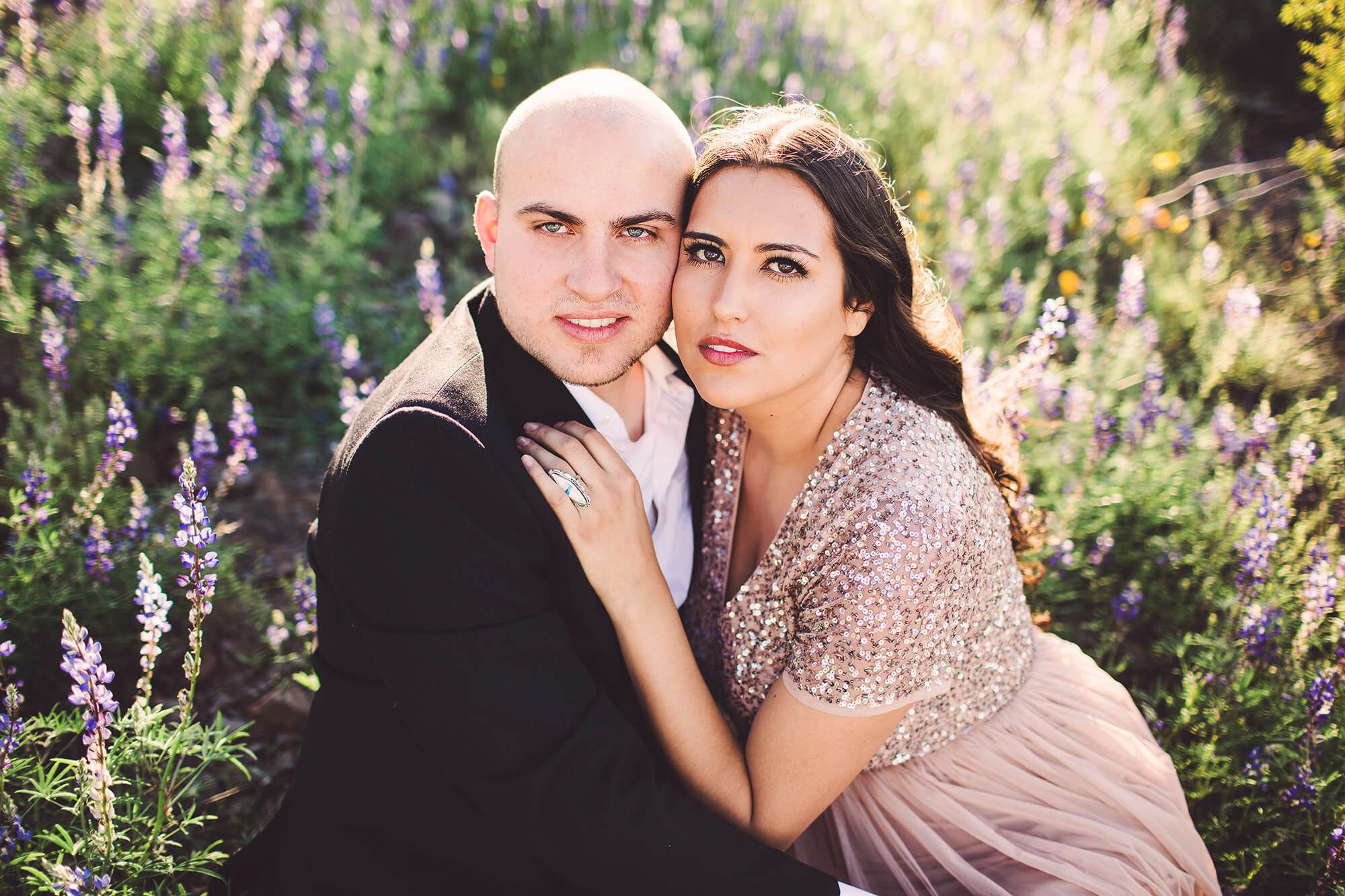 The Paxman's hold one another in the sunlight amongst the wildflowers during their couple's session with Belle Vie Photography