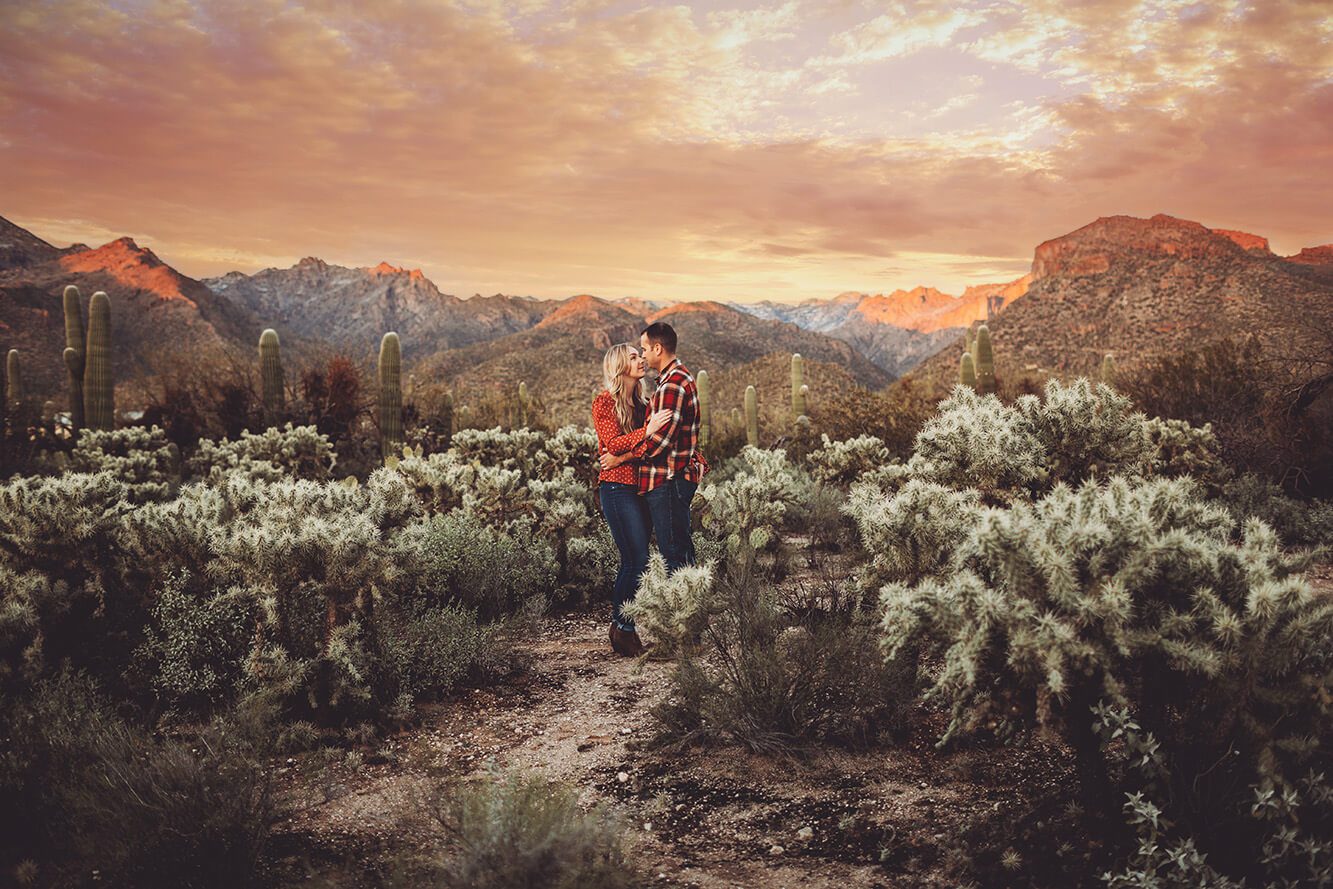 The Santa Catalina mountains glow with the setting sun as the Freeman's hold on another amongst the jumping cactus during their couple's session at Sabino Canyon