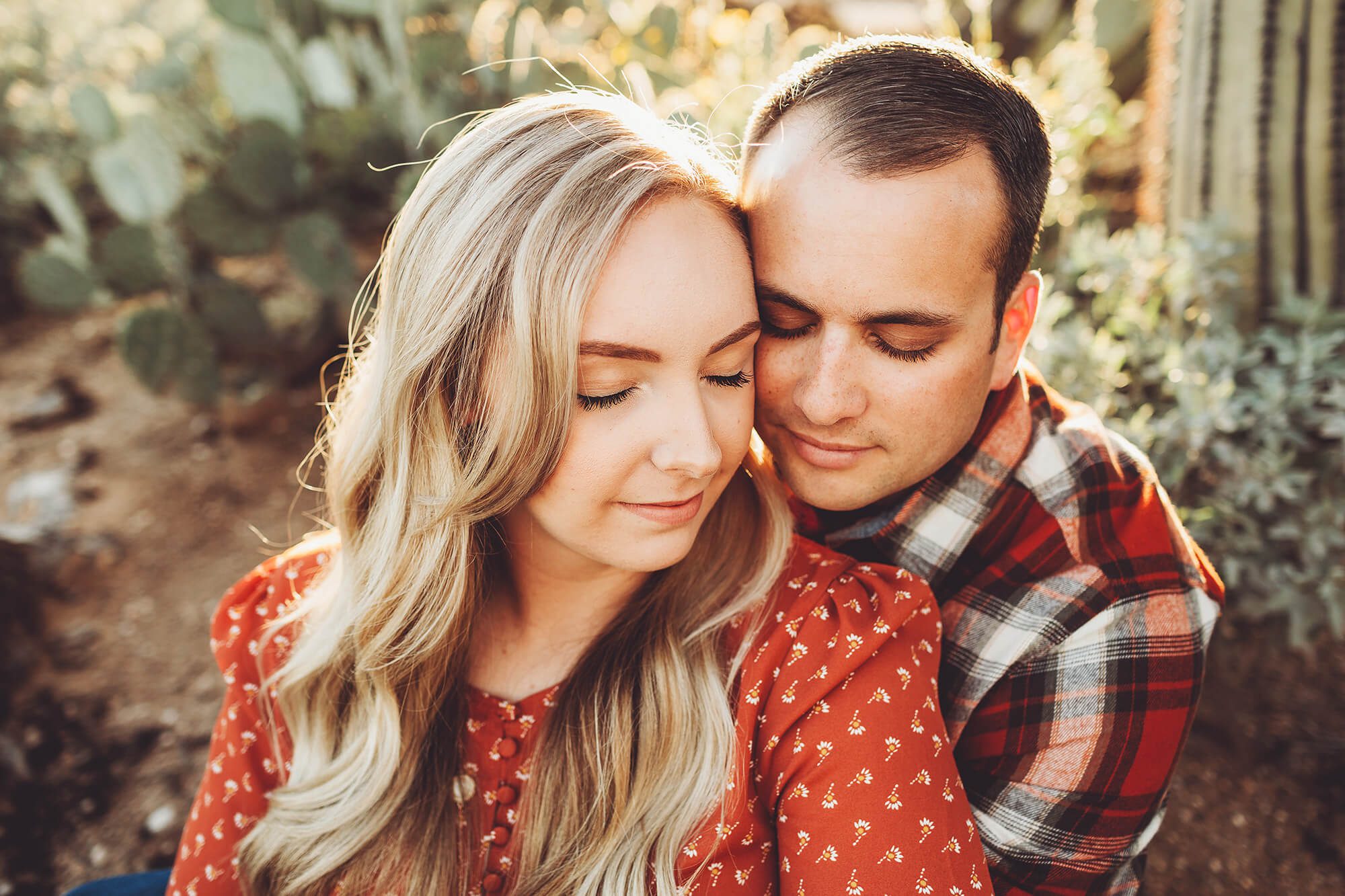 The Freeman's sit wrapped in each other's arms surrounded by cacti and sunlight during their desert couple's session at Sabino Canyon in Tucson