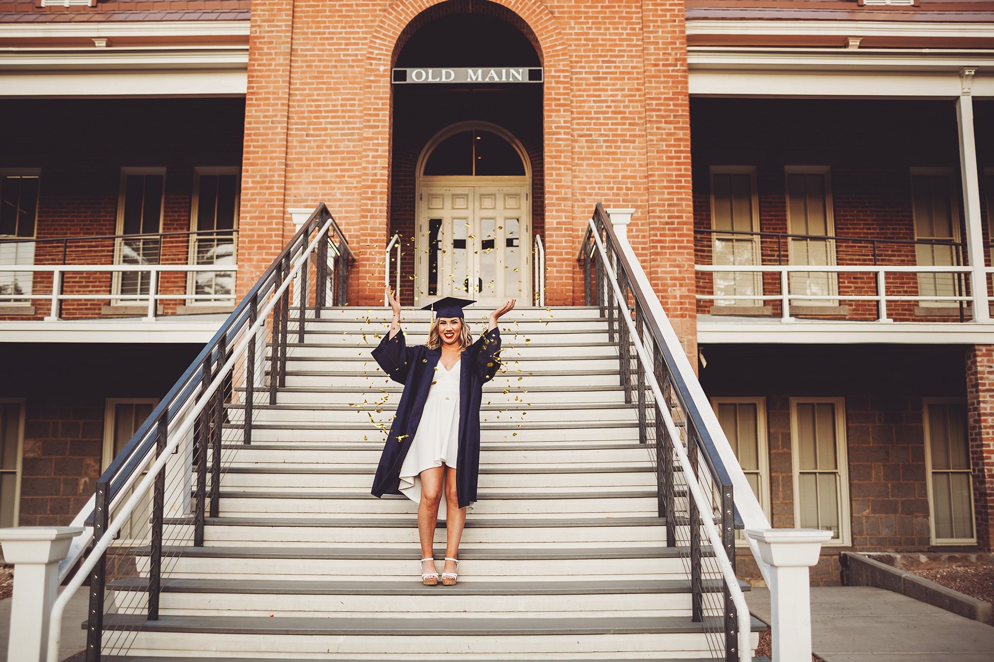 Shelby tosses confetti into the air on the steps of the Old Main building at the University of Arizona during her senior session with Belle Vie Photography