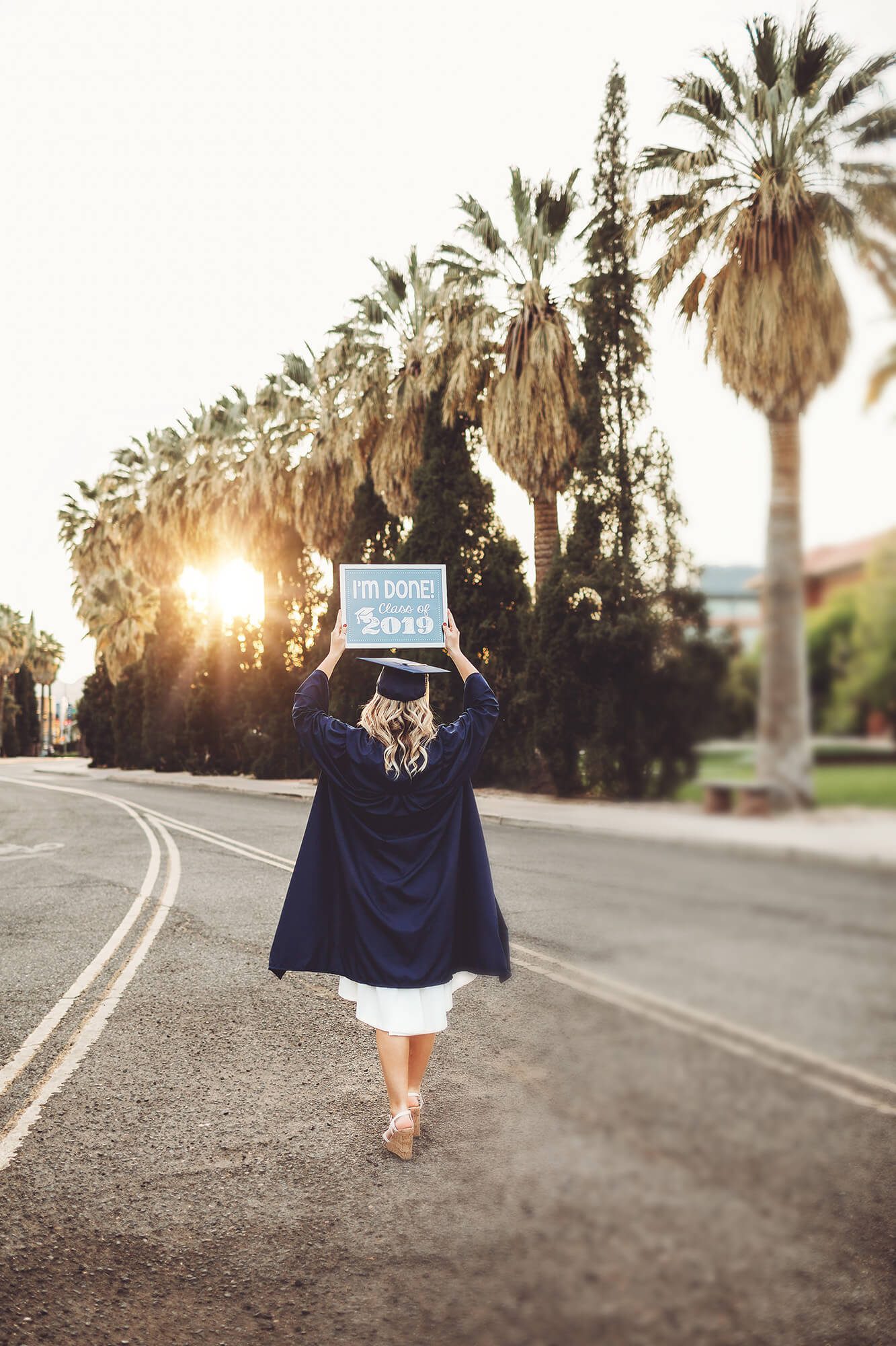 Shelby walks away from the University of Arizona holding a sign reading, "I'm Done! Class of 2019" during her graduation photo session with Belle Vie Photography.