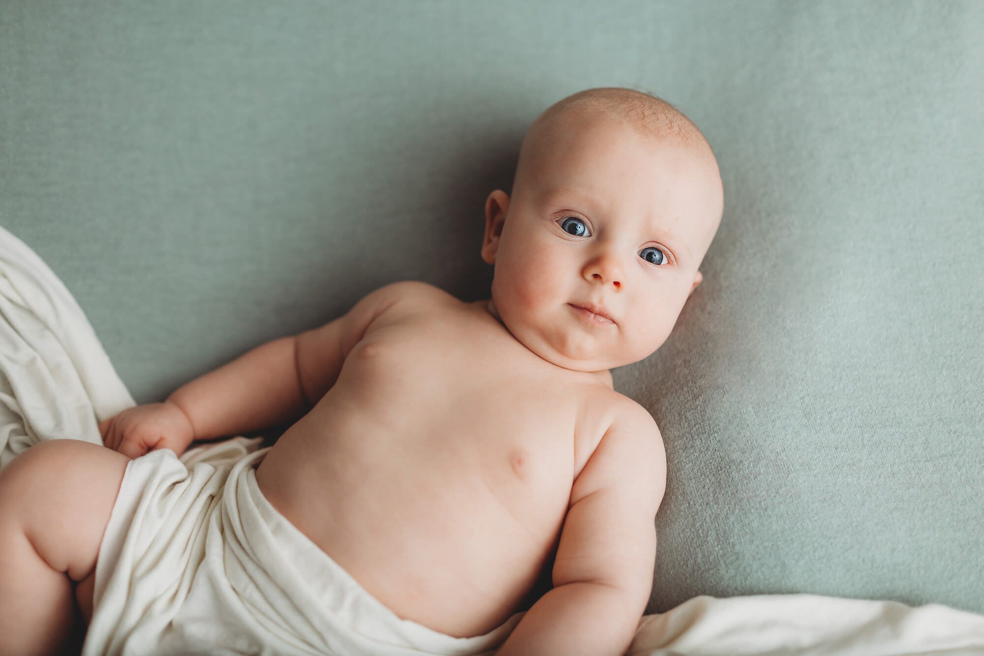 A Belle Vie Photography milestone session of a three-month old boy laying on a pale green backdrop