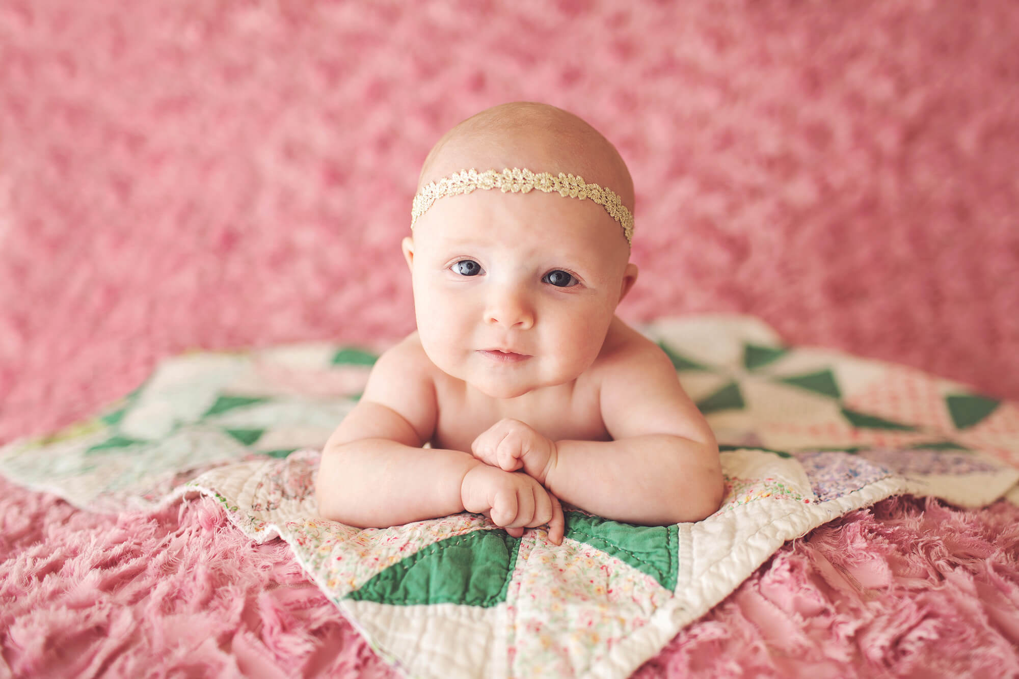 Three-month old baby girl on a pastel quilt with a golden headband
