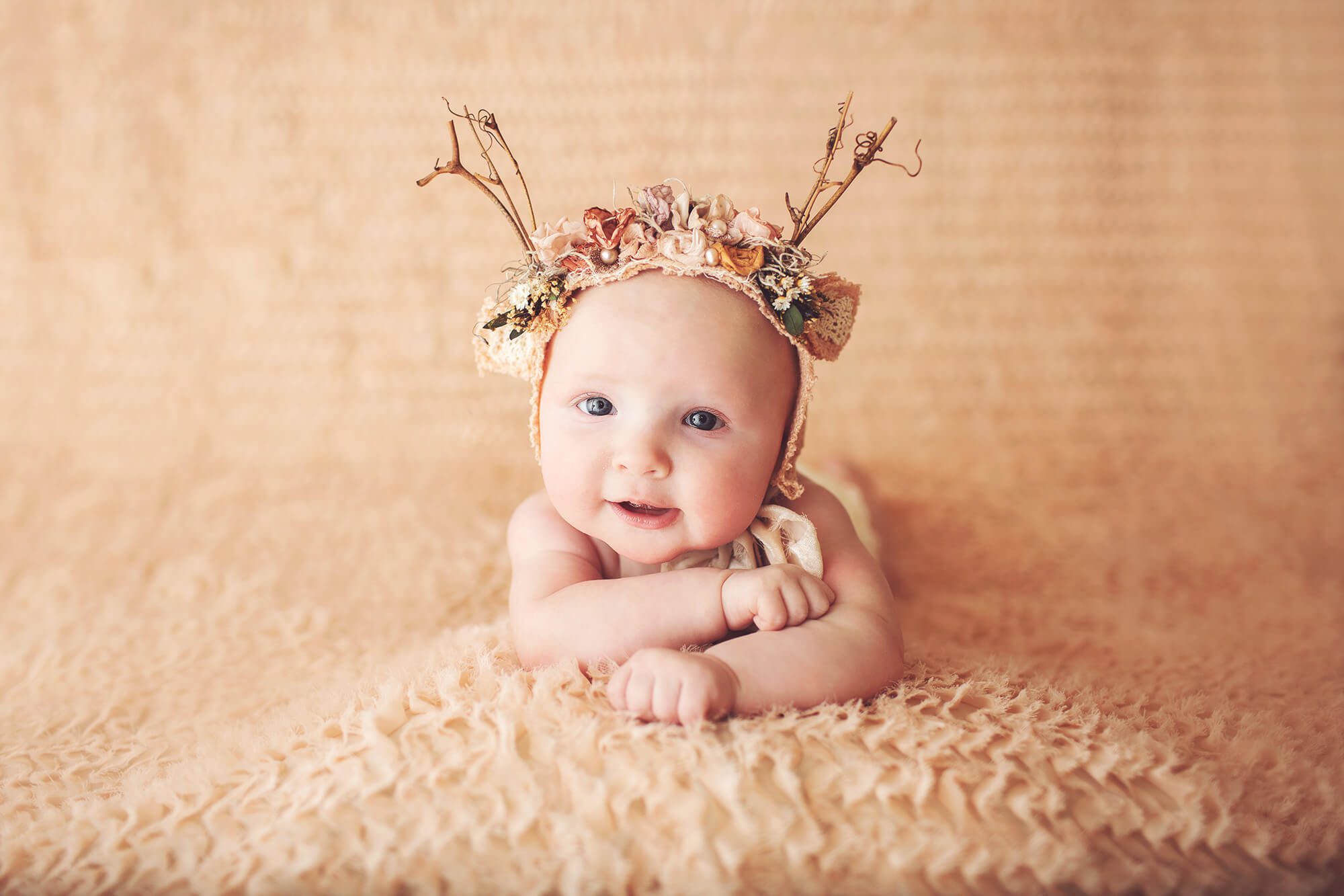 Three-month old baby girl in a peach, floral deer bonnet during her milestone session