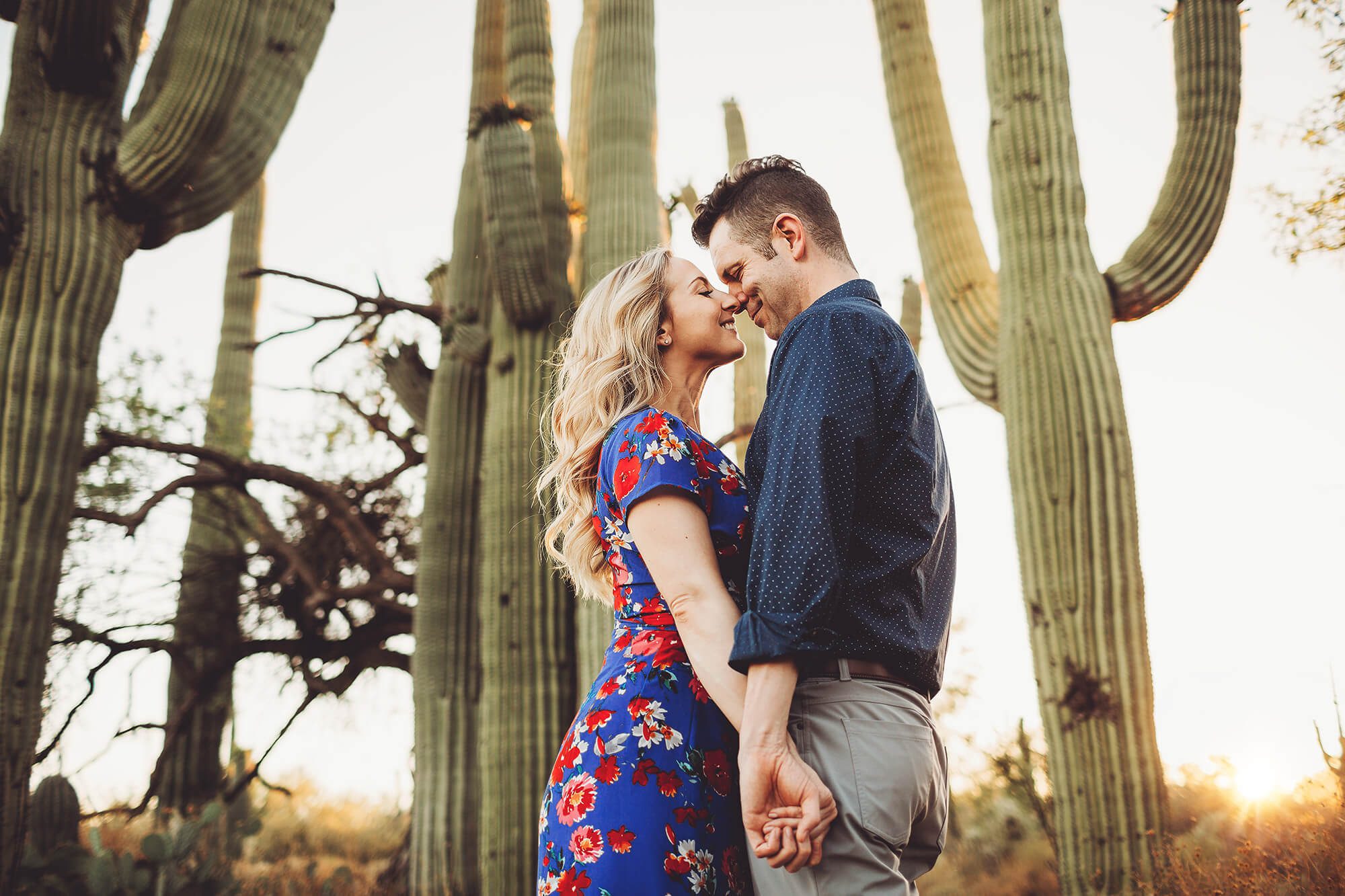 Ally and Shaun hold hands surrounded by towering saguaros during their sunset engagement session